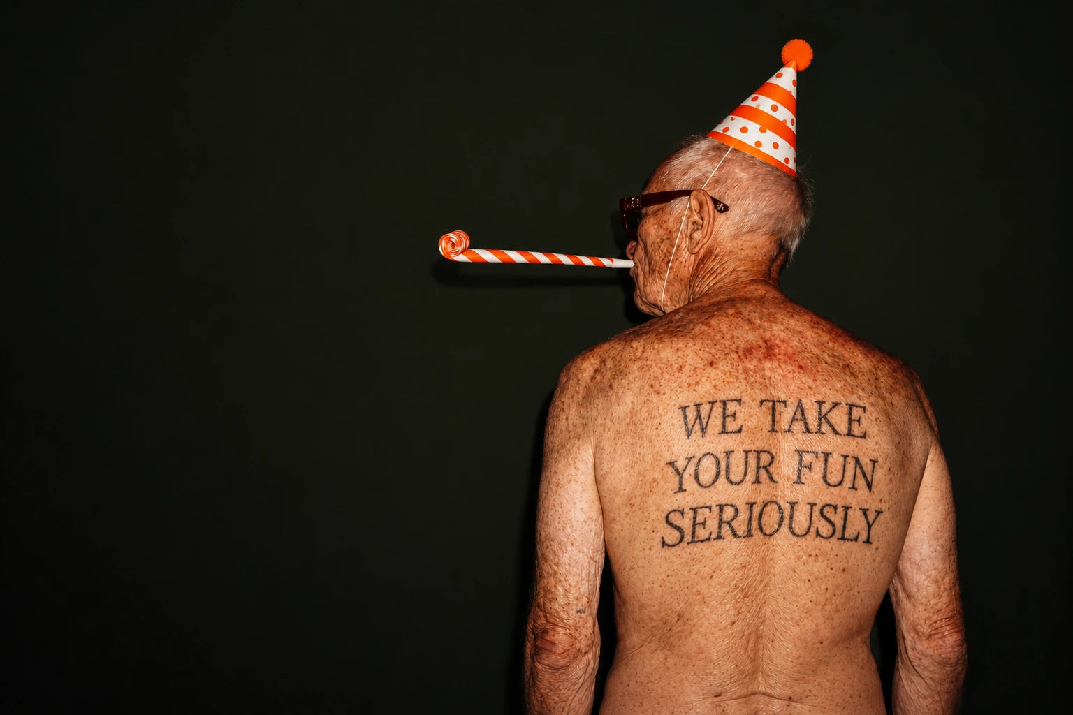 A man wearing a party hat and blowing a birthday party blower, with the words We Take Your Fun Seriously tattooed on his back.